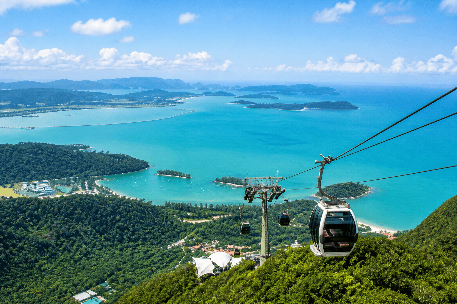 Cable car cabins gliding above lush green mountains in Langkawi, offering panoramic views of tropical forests, coastline, and turquoise sea.